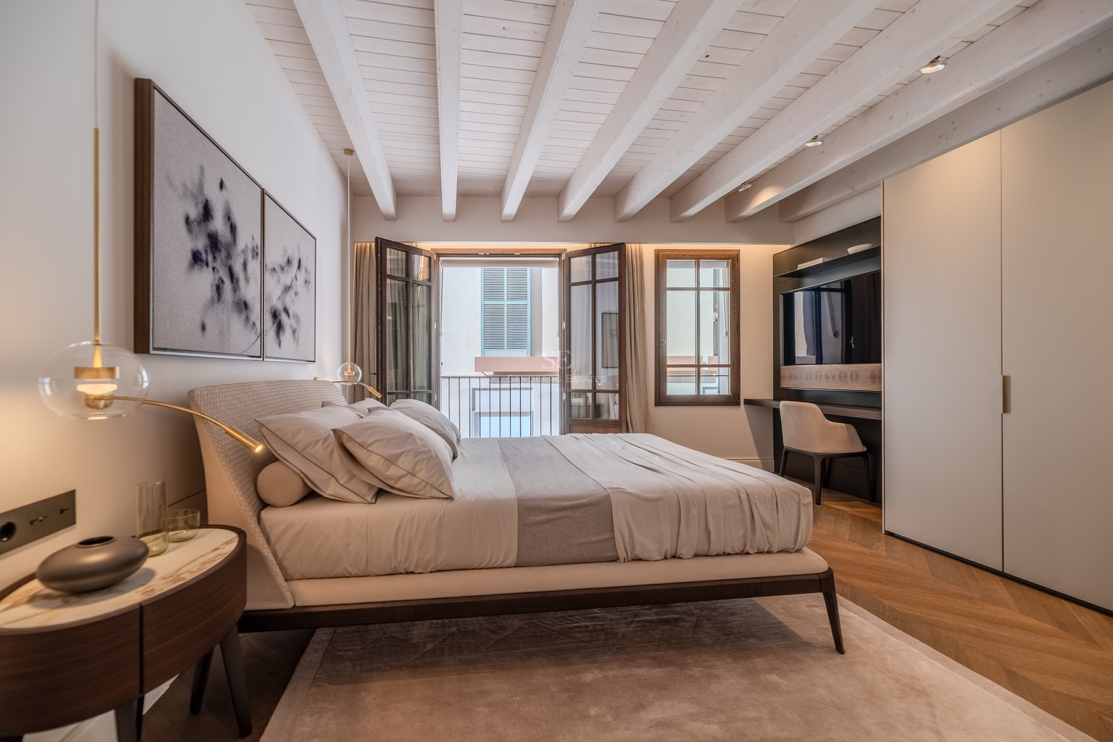 Chambre élégante avec plafond à poutres blanches, parquet en point de Hongrie et balcon donnant sur une rue.