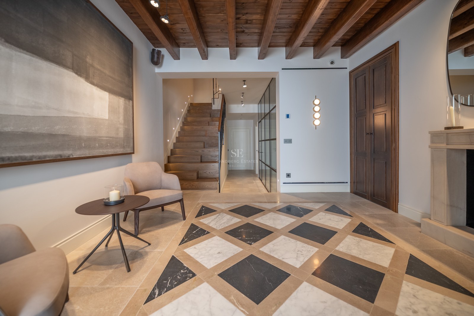 Hall d'entrée de luxe avec sol en marbre géométrique, poutres en bois, escalier en chêne et cheminée en pierre.