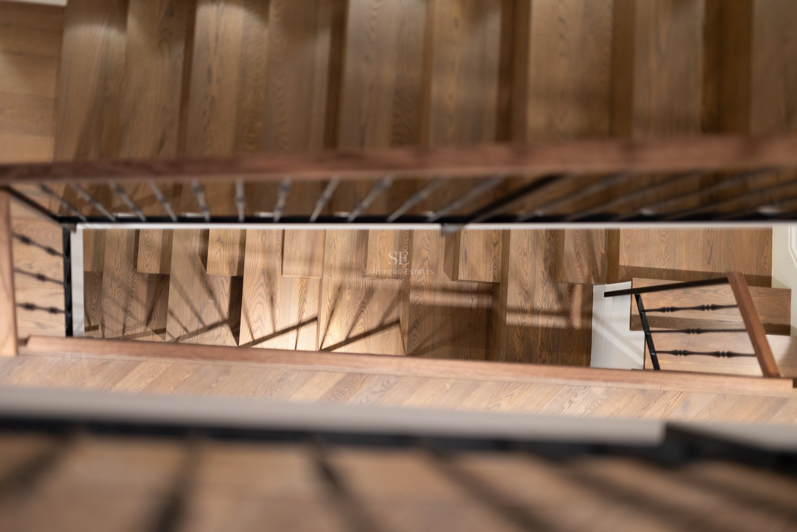 Vue de dessus d'un escalier en bois de chêne avec une rampe en fer forgé noir dans une propriété de luxe.