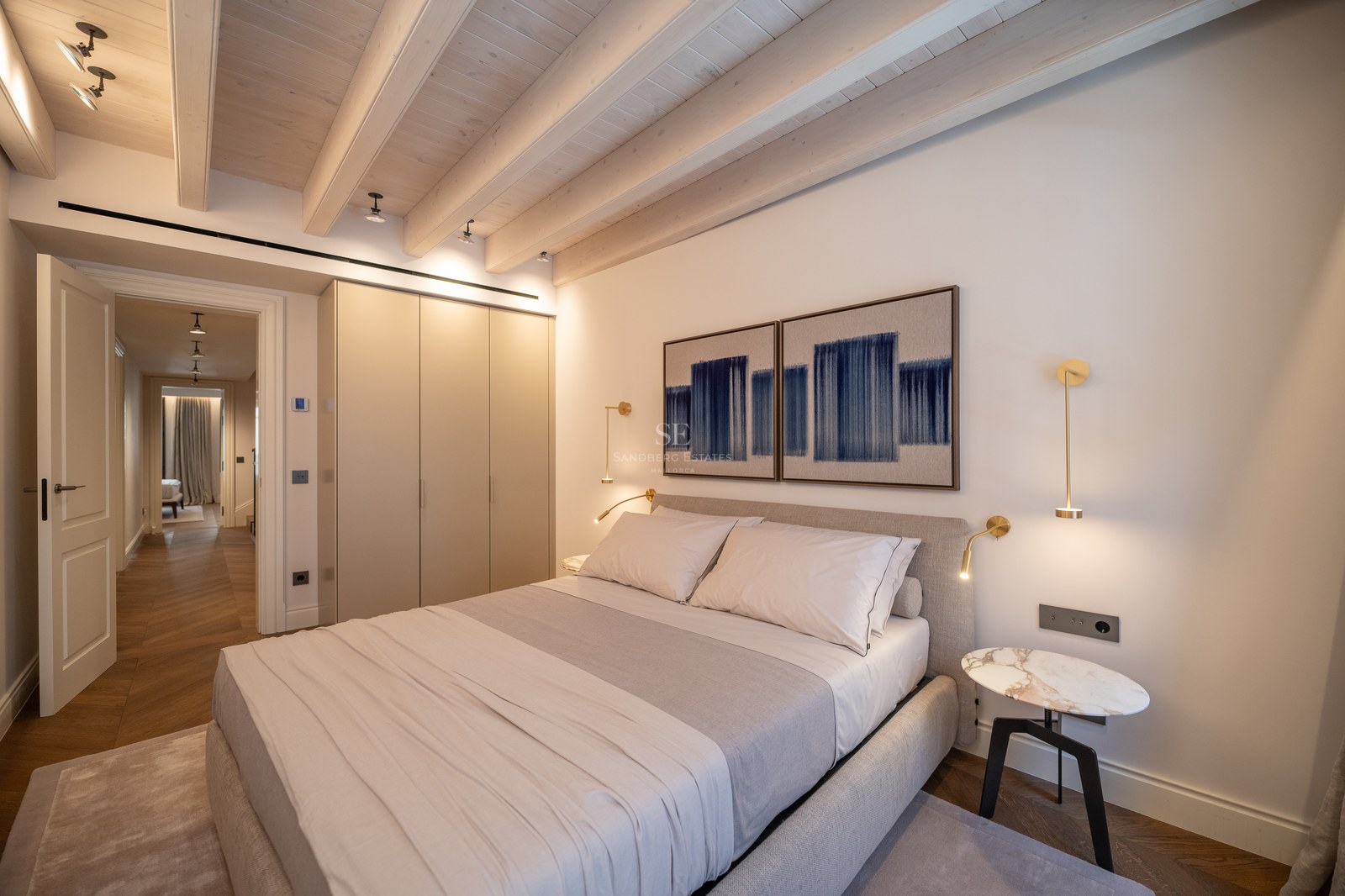 Chambre moderne avec poutres en bois blanchi, armoires encastrées et appliques en laiton.