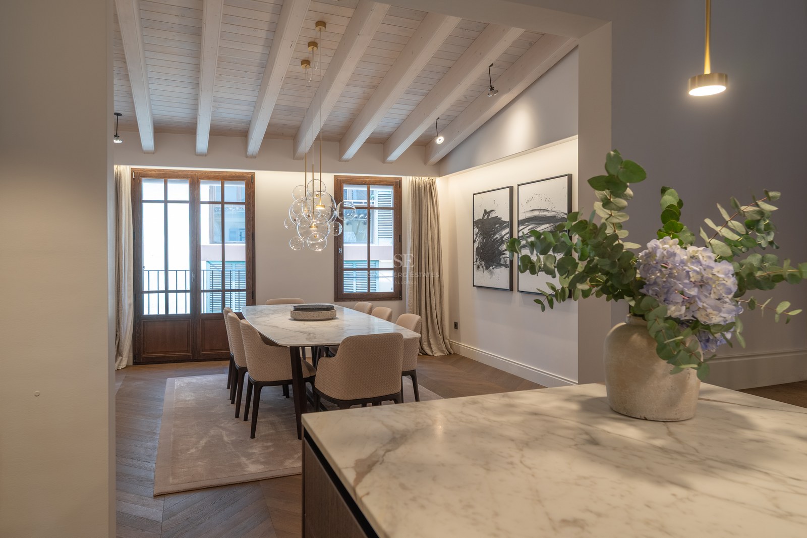 Salle à manger moderne avec table en marbre, chaises rembourrées, plafond à poutres et parquet en chevrons.