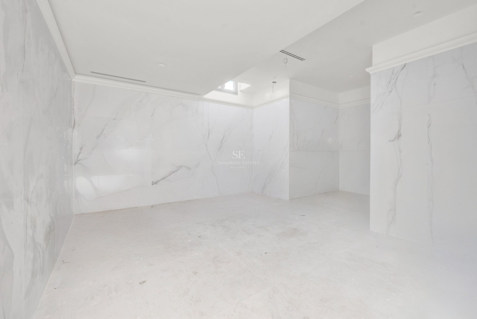 Baño de lujo en construcción con paredes y suelos de mármol blanco con vetas grises y techos con aire integrado.