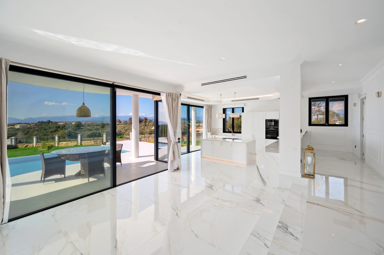 Salón moderno con suelos de mármol blanco y ventanales de suelo a techo que dan a una terraza con piscina.