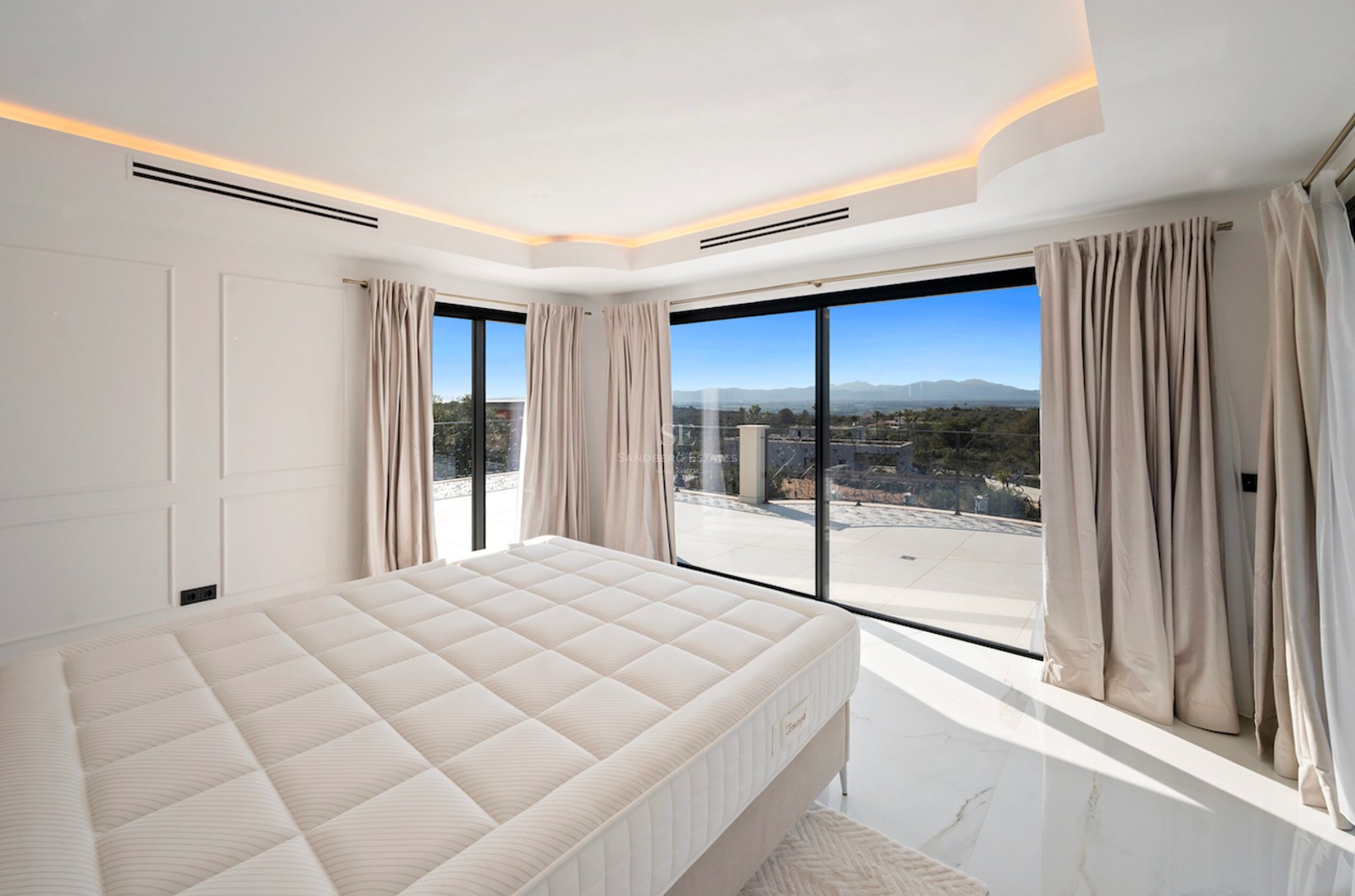 Dormitorio principal moderno con suelo de mármol y ventanales que dan a una terraza con vistas a la montaña.