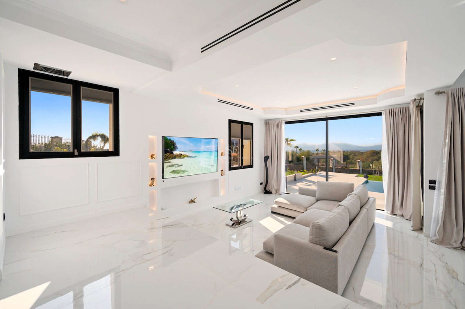 Salón contemporáneo luminoso con suelos de mármol blanco, grandes puertas correderas de cristal y TV de pared.