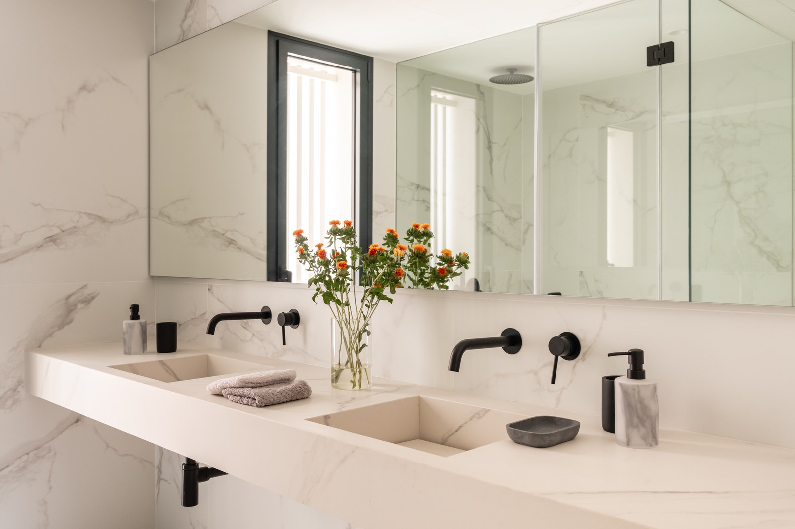 Modern master bathroom featuring a double marble vanity, integrated sinks, matte black faucets, and large wall mirror.