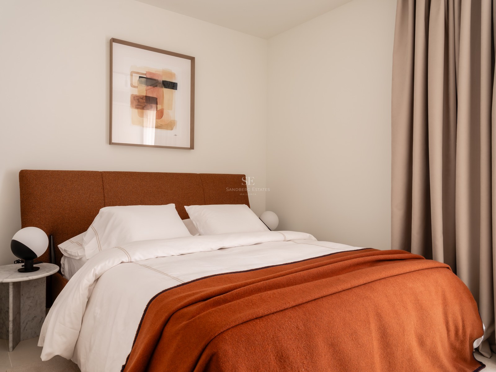 Modern bedroom featuring a burnt orange headboard, marble side table, and abstract wall art in soft natural light.