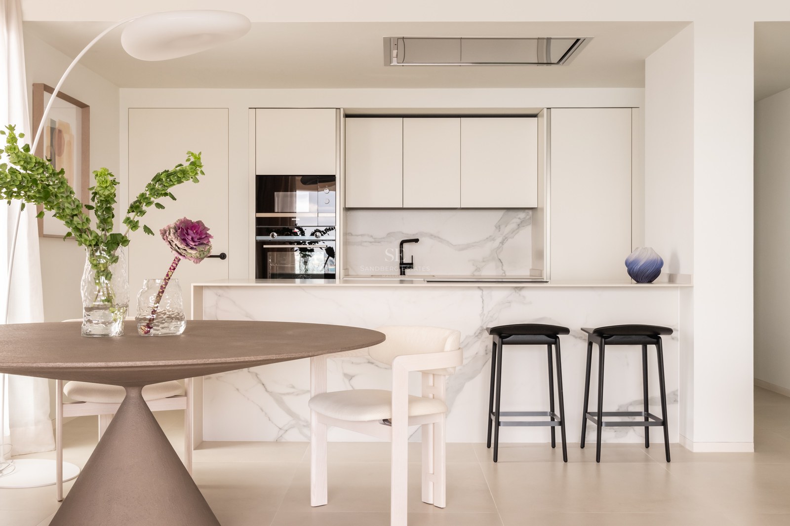 Minimalist kitchen featuring a Calacatta marble island, integrated appliances, and dining area with a round table.