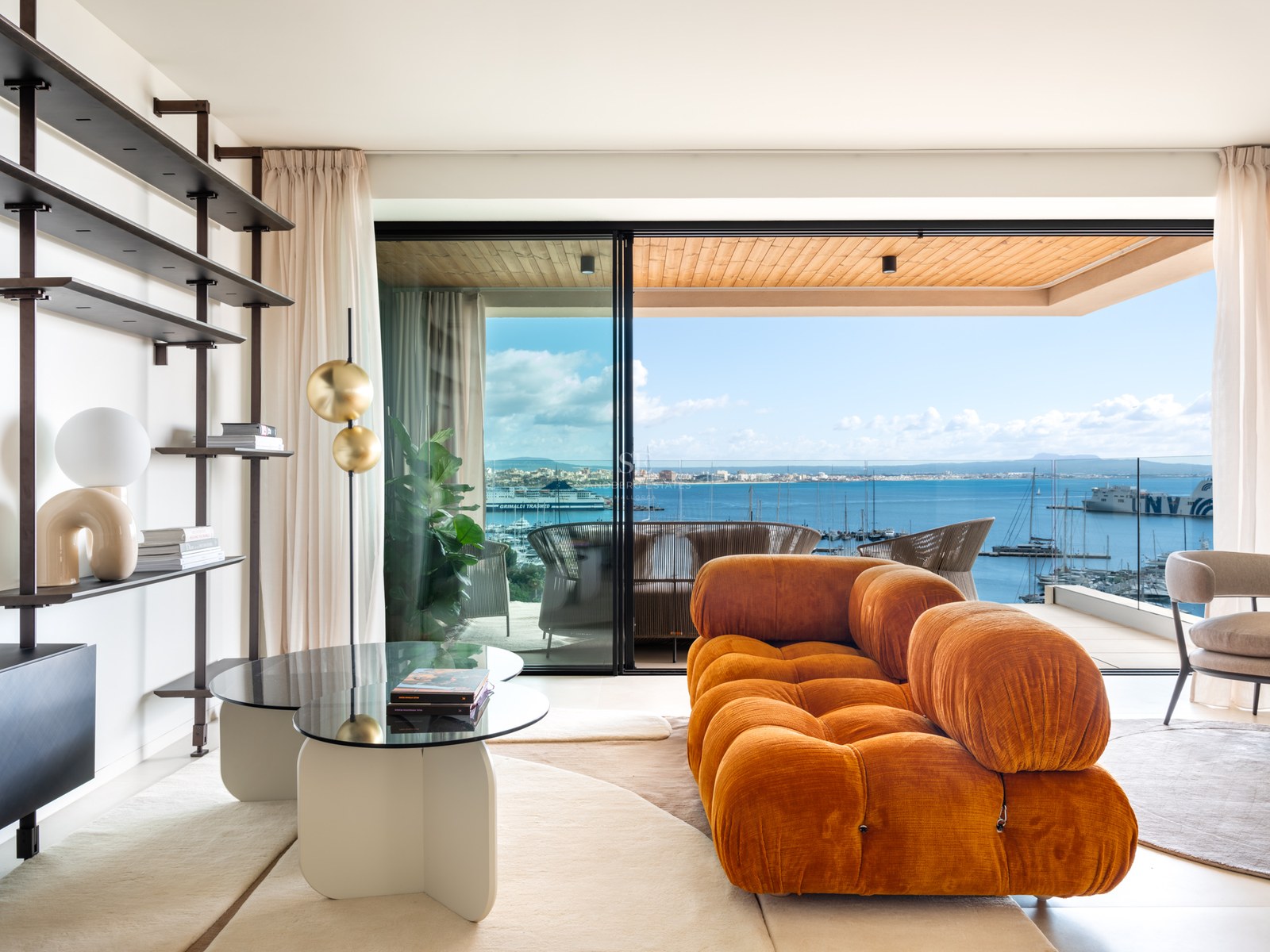Contemporary living room with a terracotta velvet sofa and floor-to-ceiling windows overlooking a Mediterranean marina.