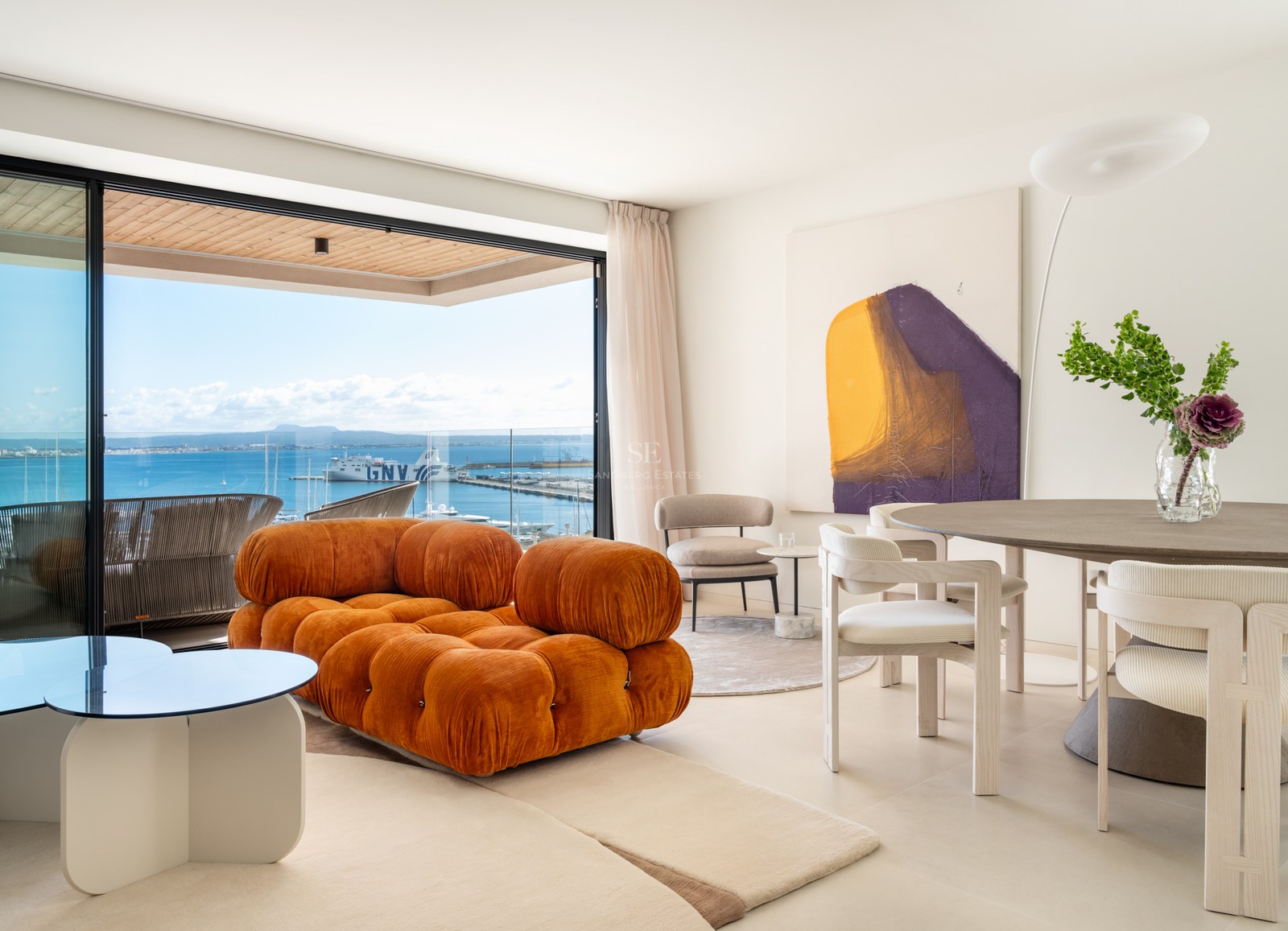 Modern living room with a burnt orange modular sofa, dining area, and large sliding doors opening to a sea-view terrace.