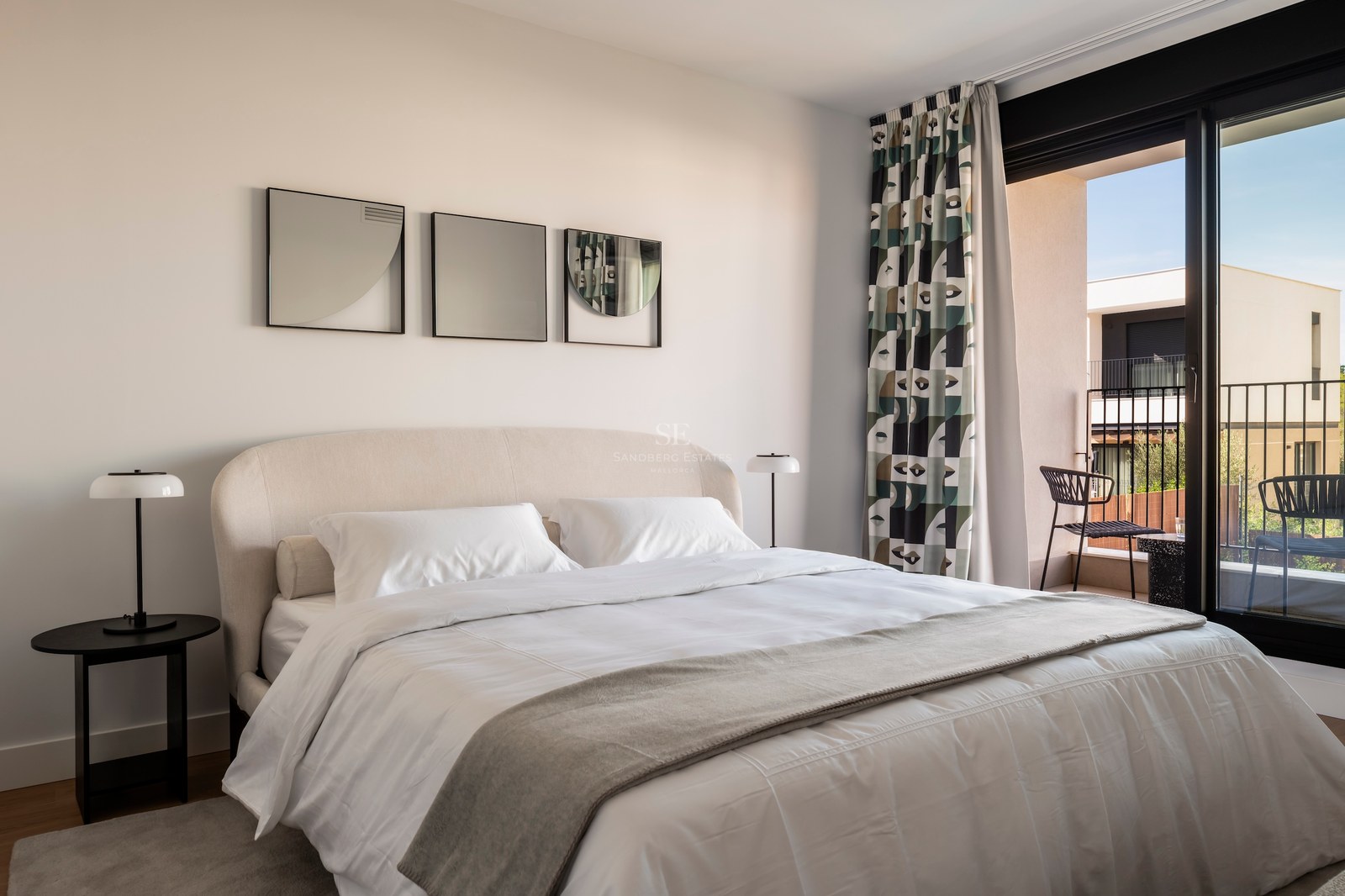 Chambre moderne avec lit rembourré, lampes design et baies vitrées ouvrant sur une terrasse.