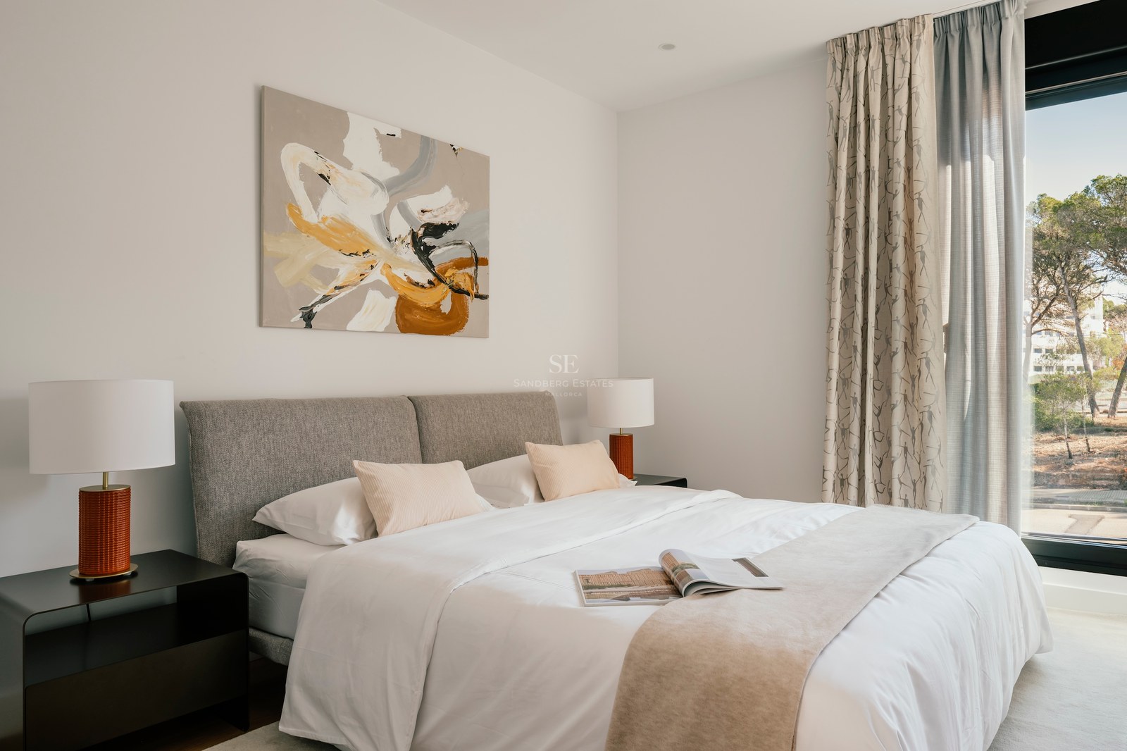 Chambre moderne avec tête de lit grise, linge blanc, art abstrait et grande baie vitrée.