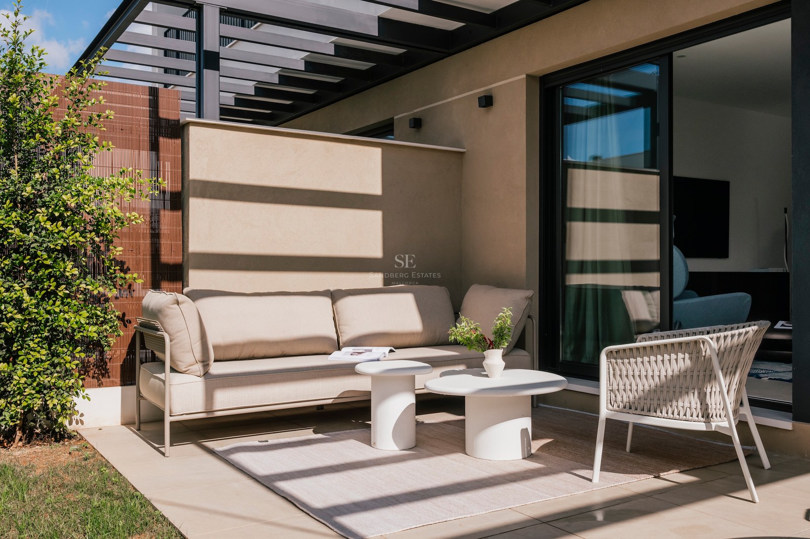 Terrasse moderne avec canapé beige, tables basses blanches et fauteuil tressé sous une pergola architecturale.