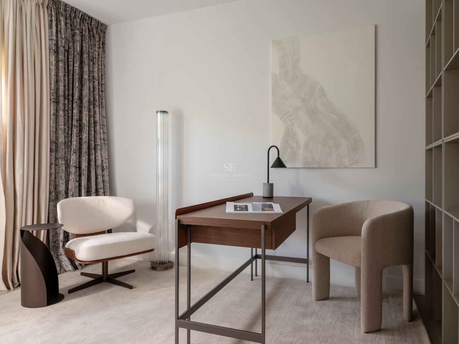 Bureau moderne avec table en noyer, fauteuil beige sculptural et œuvre d'art texturée dans une pièce lumineuse.