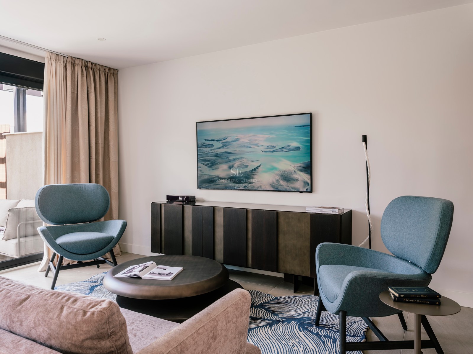 Espace salon moderne avec deux fauteuils bleu sarcelle, une table basse ronde et un meuble TV en bois sombre.