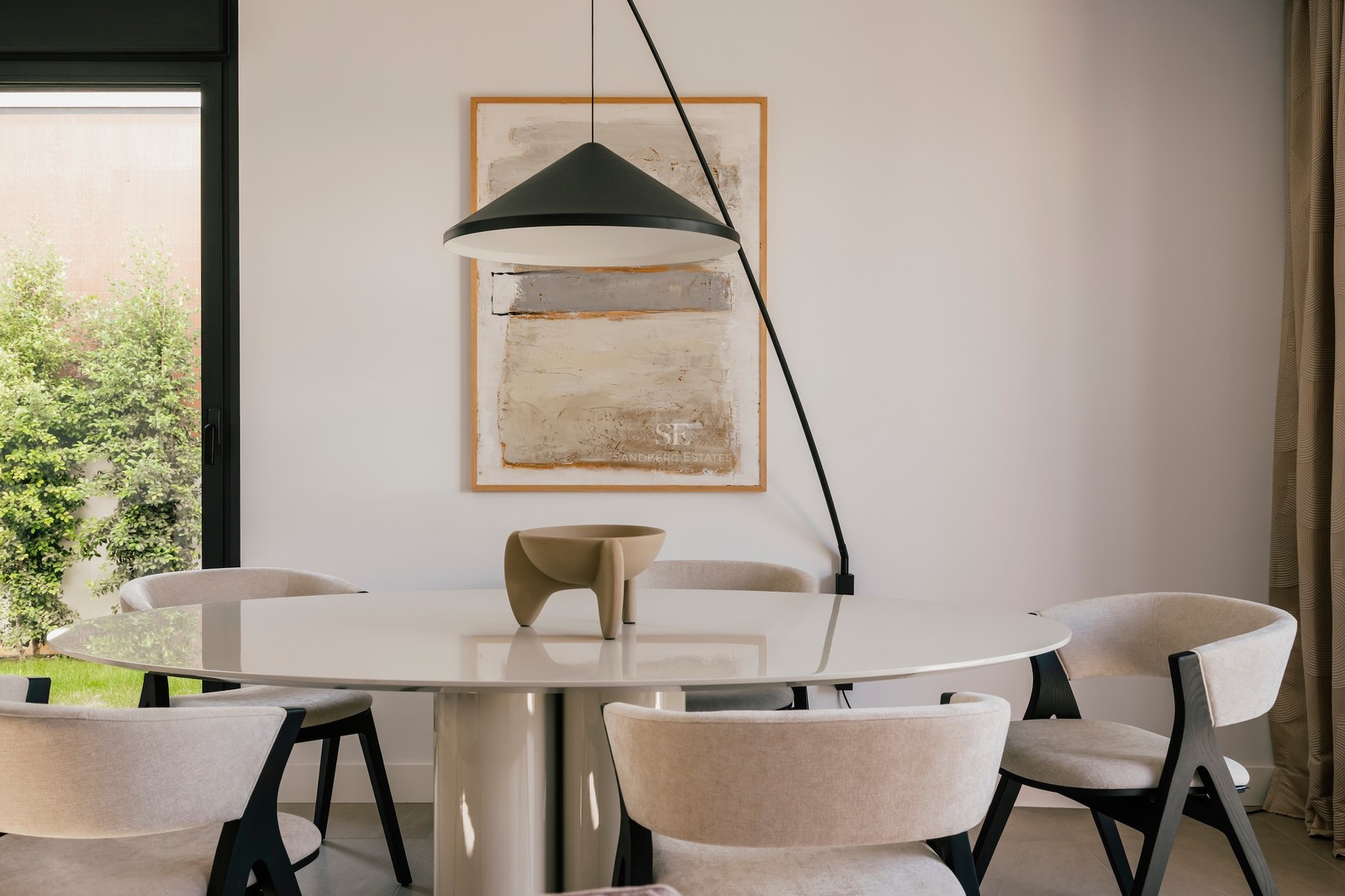 Une table à manger ronde blanche avec six chaises en tissu beige sous une suspension design noire.