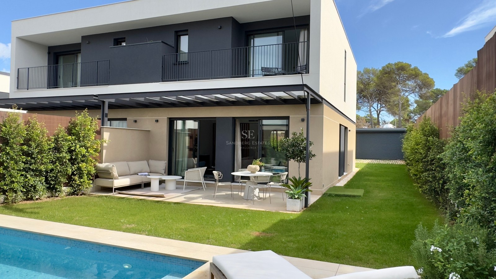 Extérieur d'une villa moderne blanche et grise avec terrasse, pelouse et piscine bleue au premier plan.
