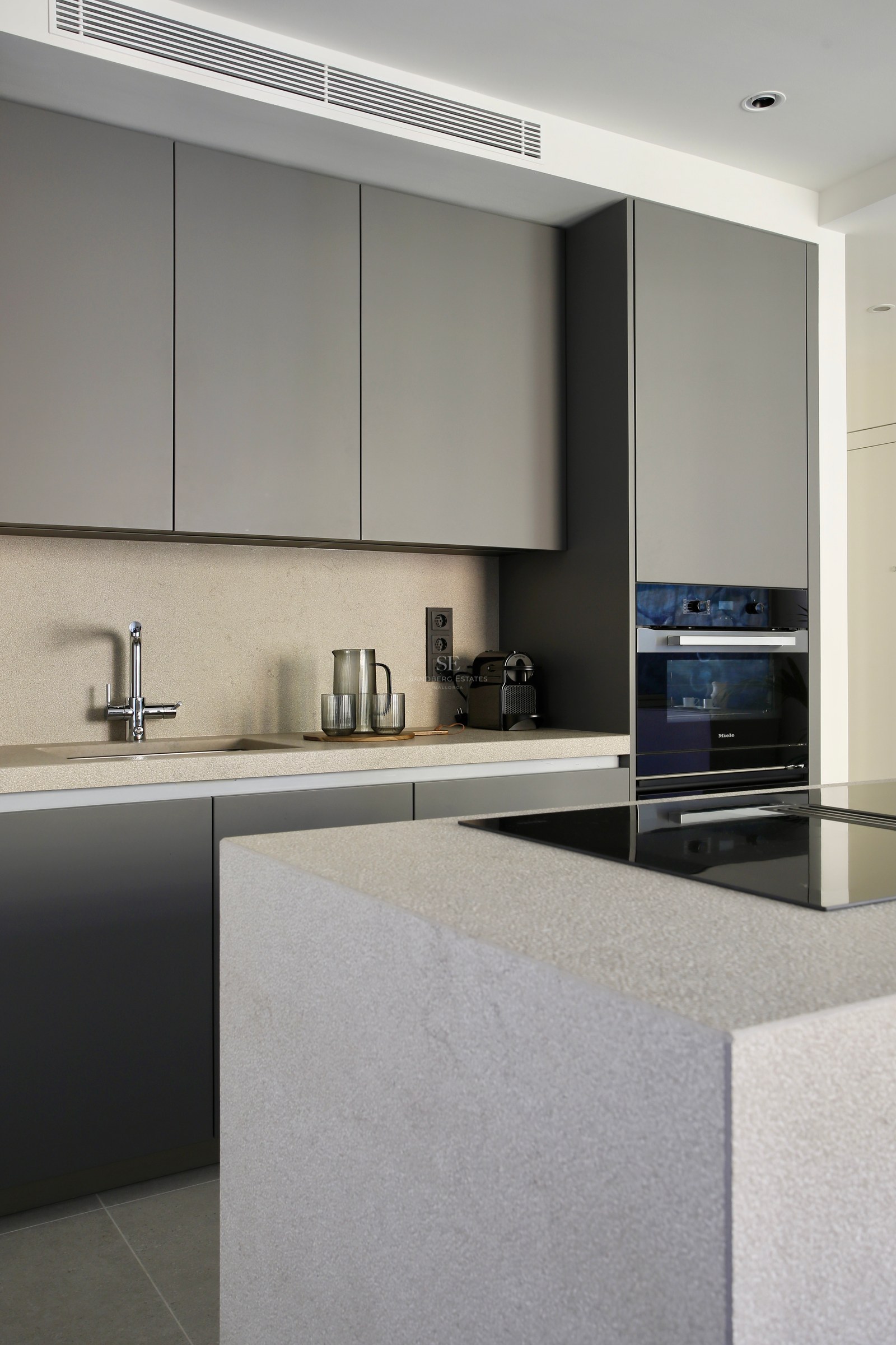 Minimalist kitchen featuring matte grey cabinetry, sand-colored stone countertops, and an integrated Miele oven.