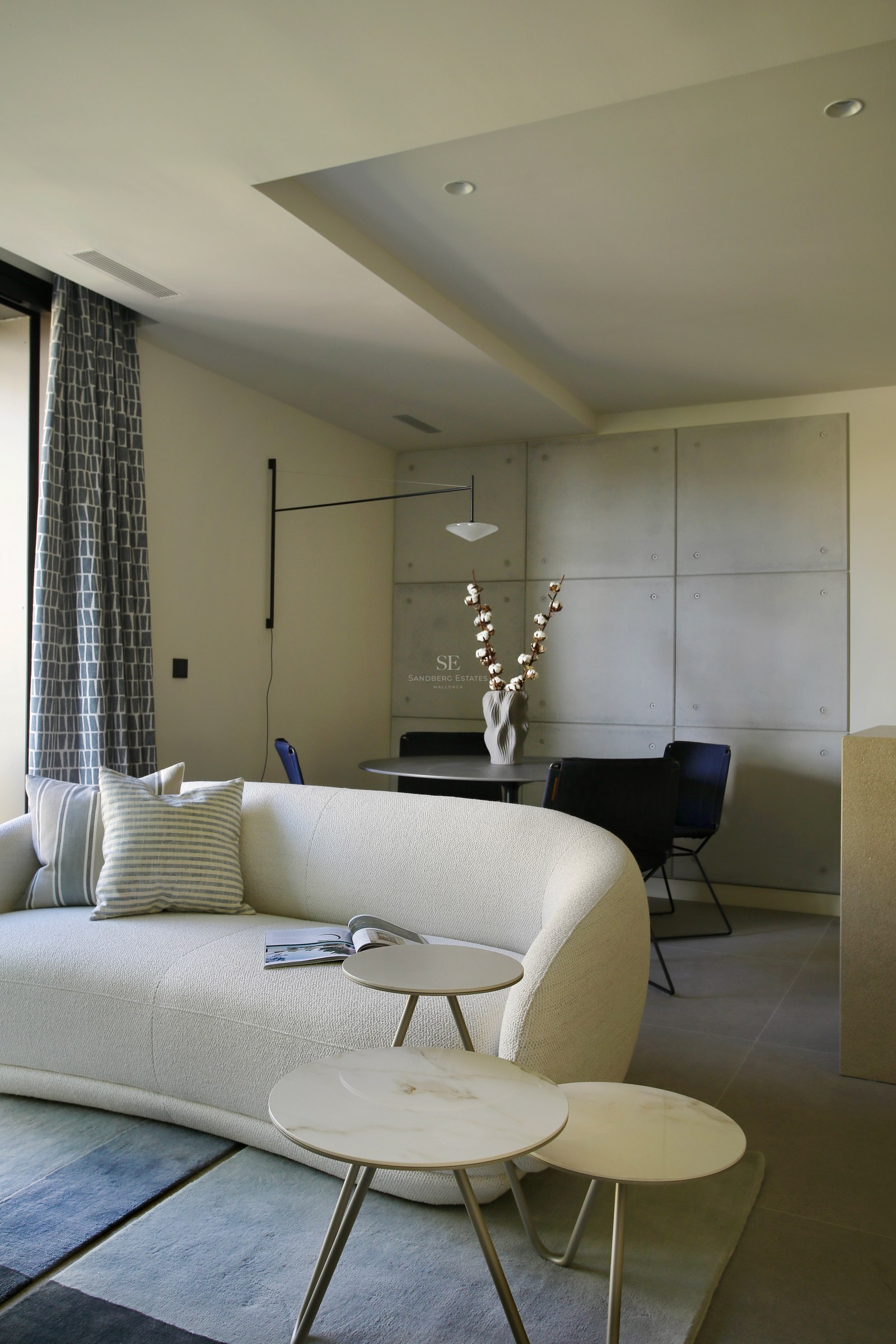 Modern living room featuring a curved white bouclé sofa, marble coffee tables, and a concrete-paneled accent wall.