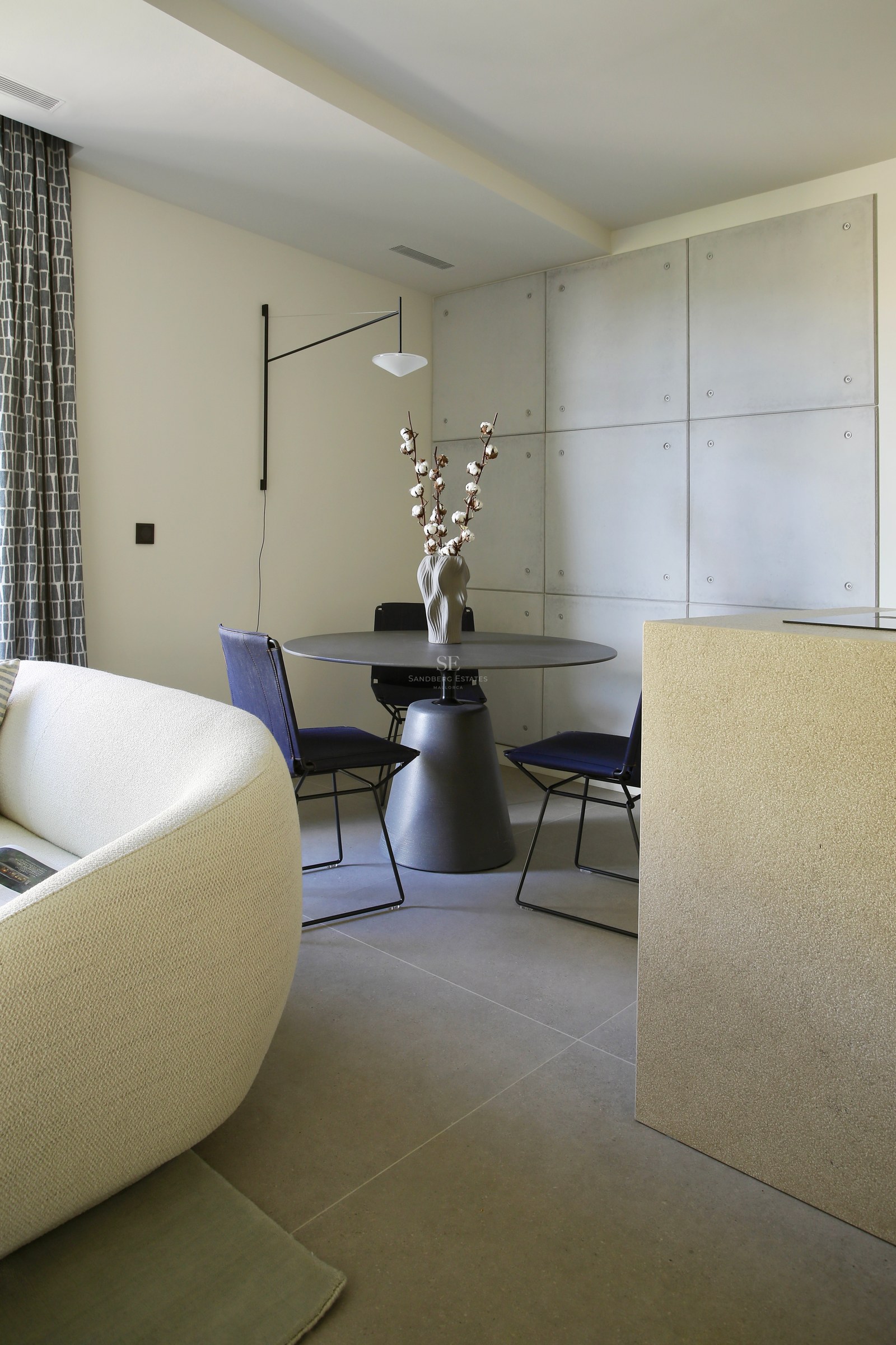 Modern dining space featuring a round table, navy chairs, and concrete panel wall next to a curved bouclé sofa.