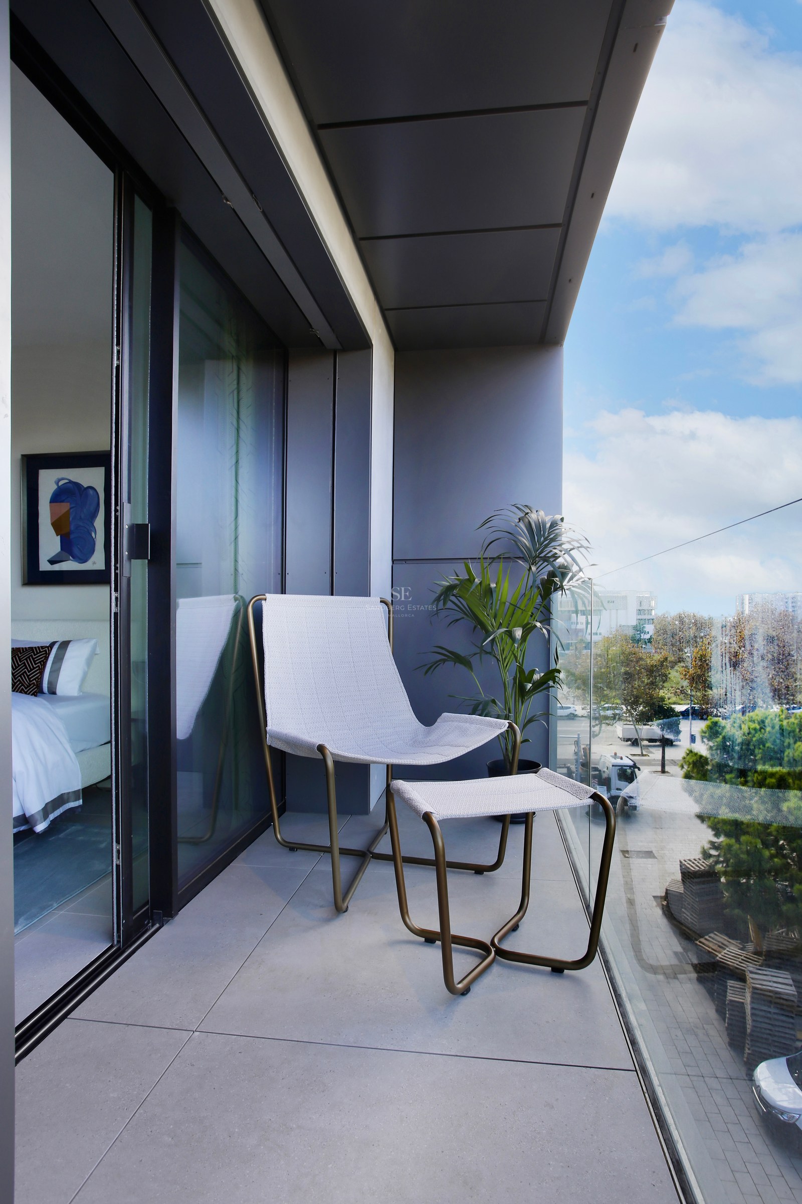 Contemporary balcony featuring a designer lounge chair, glass balustrade, and floor-to-ceiling sliding glass doors.