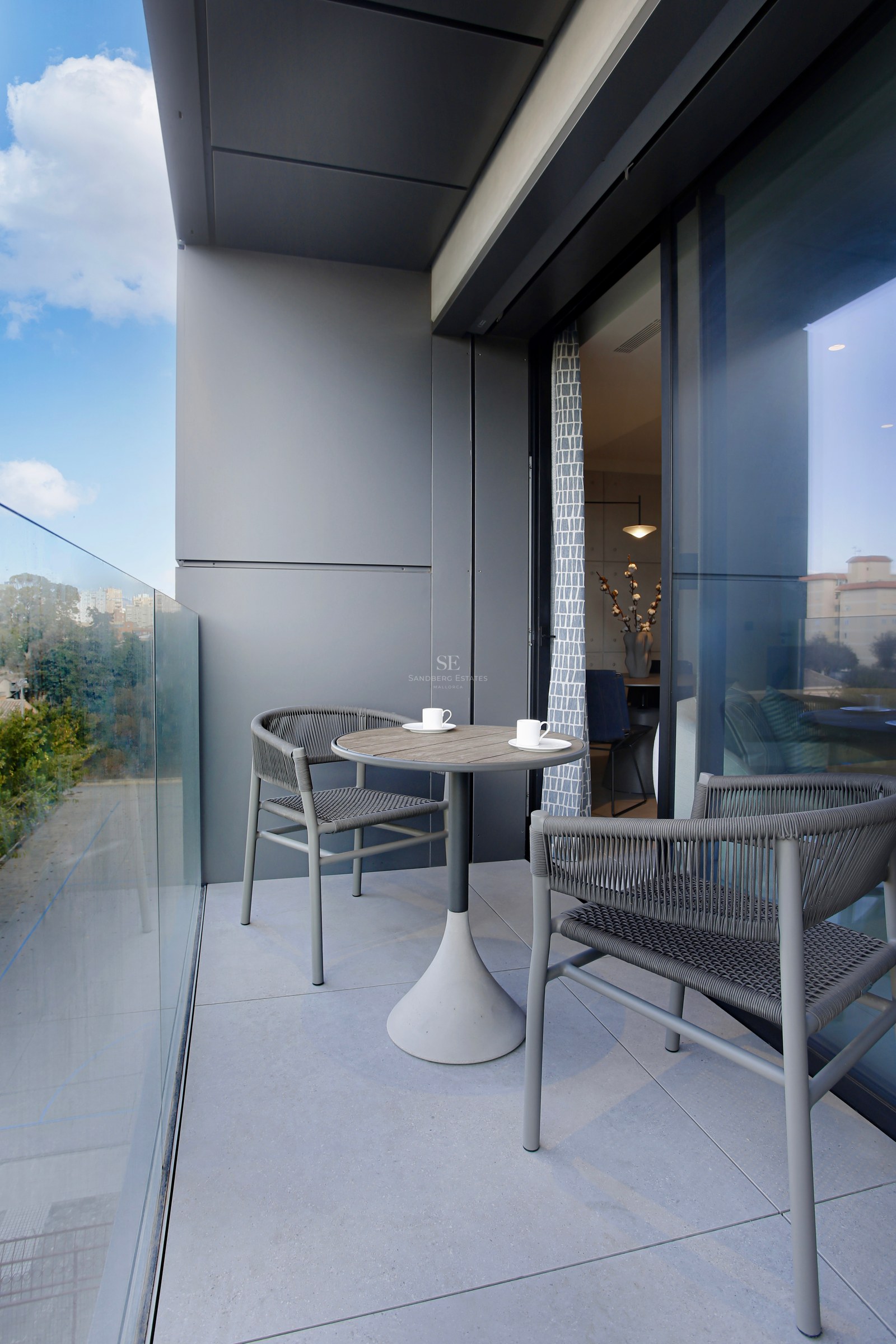 Modern balcony featuring a glass balustrade, two grey woven chairs, and a round pedestal table.