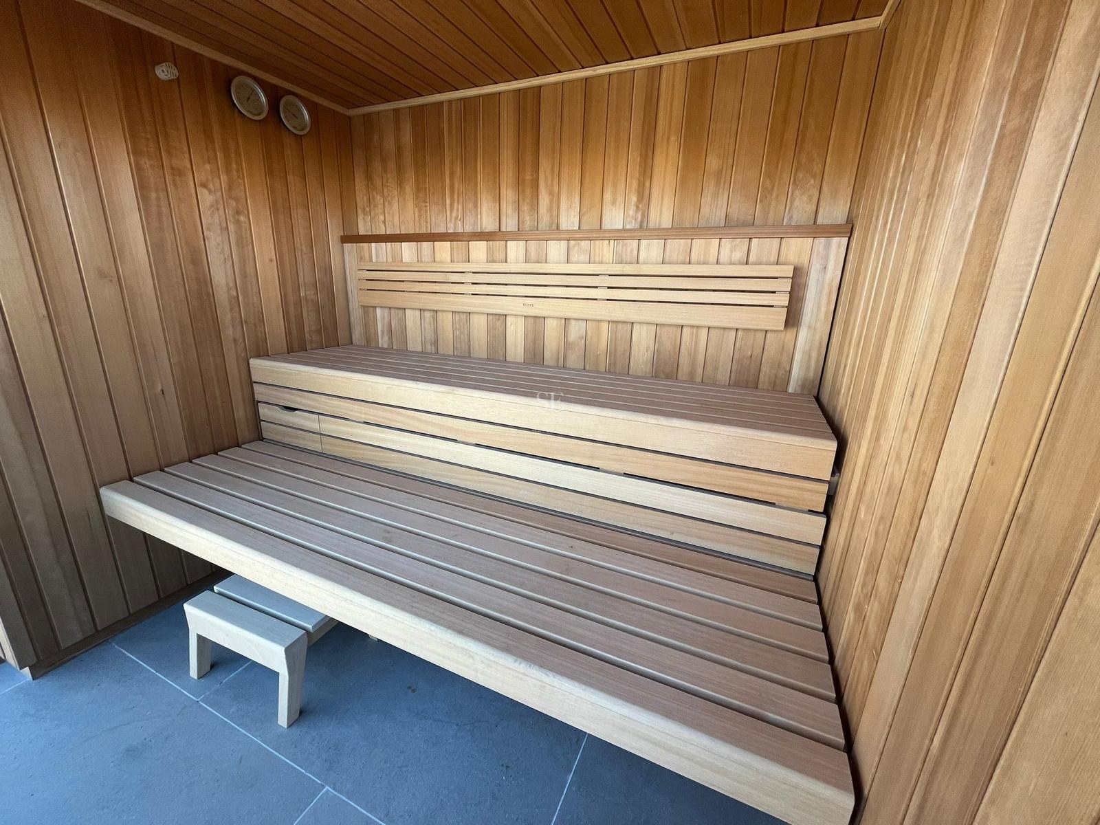 Interior view of a modern wooden sauna featuring two-tiered slatted benches and grey floor tiles.