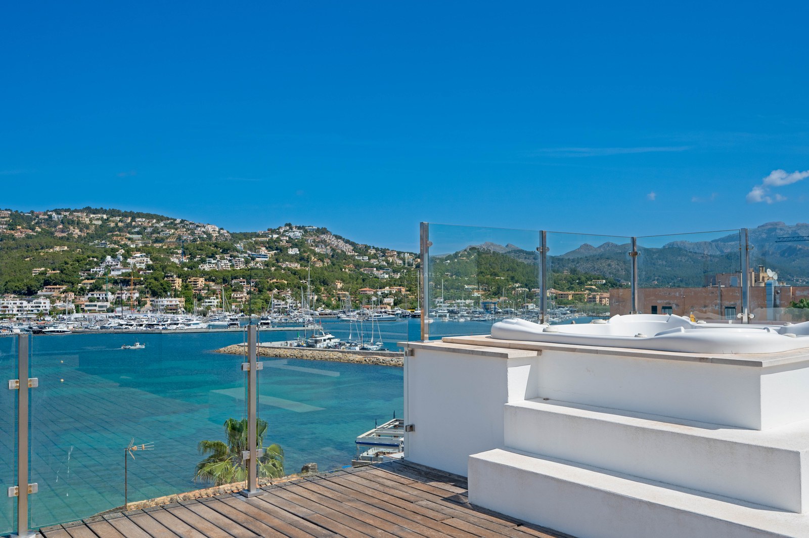 Weißer Jacuzzi auf einer Dachterrasse mit Blick auf eine Bucht mit Yachten und Küstenhügeln.