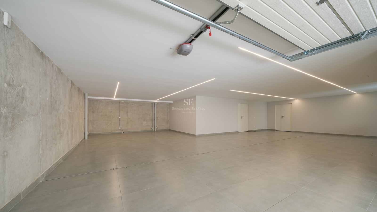 Garaje subterráneo minimalista con suelos de baldosa gris, paredes de hormigón y luces LED lineales en el techo.