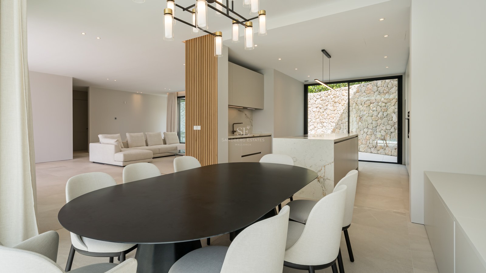 Comedor contemporáneo con mesa negra, sillas blancas, isla de cocina de mármol y pared decorativa de madera.