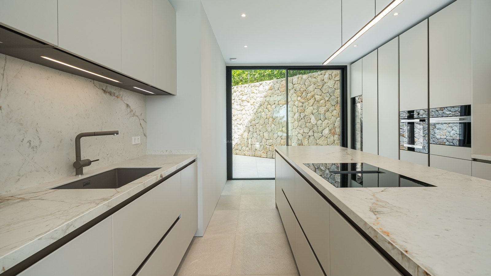 Cocina moderna minimalista con armarios blancos, encimeras de mármol y puerta de cristal de suelo a techo.