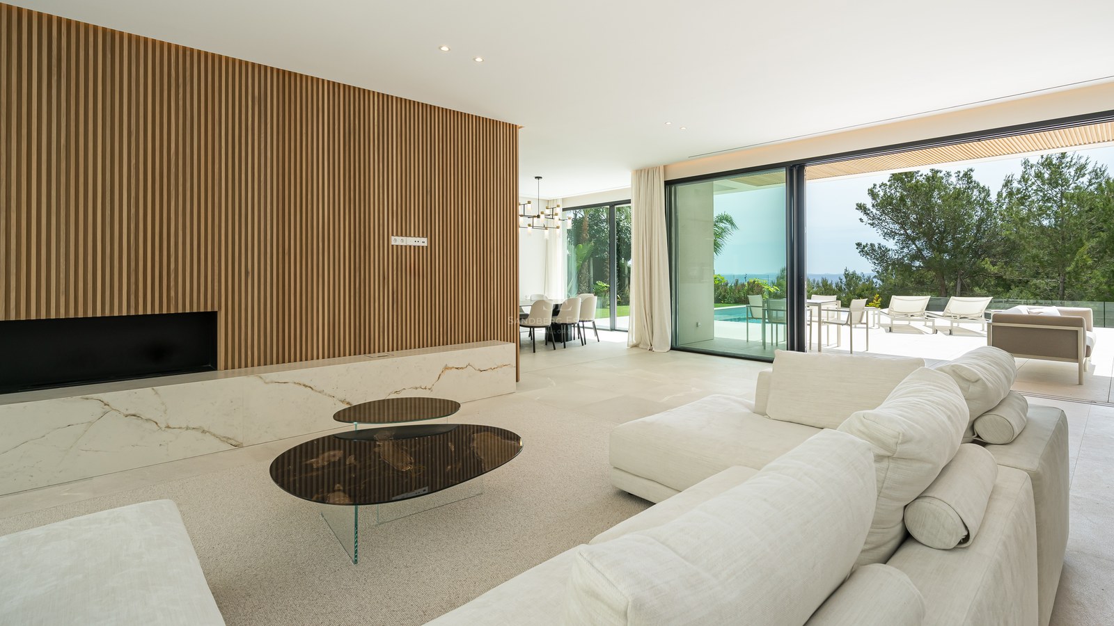 Salón contemporáneo con pared de listones de madera, chimenea de mármol y ventanales que dan a una terraza con piscina.