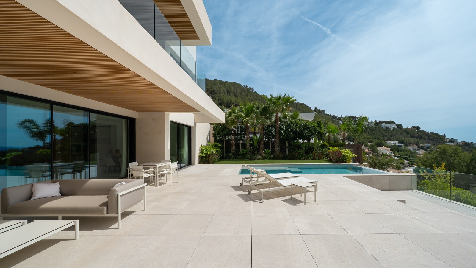 Terraza de villa de lujo con piscina grande, muebles de exterior contemporáneos y vistas panorámicas a la costa.