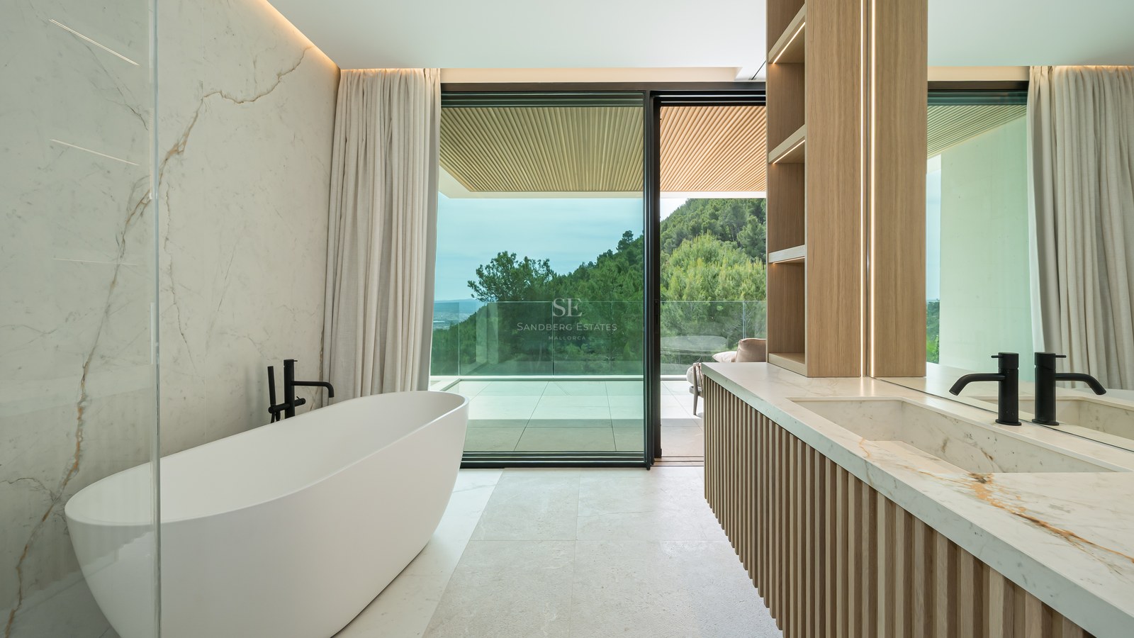 Baño moderno con bañera exenta, paredes de mármol y ventanales con vistas a un bosque de pinos.
