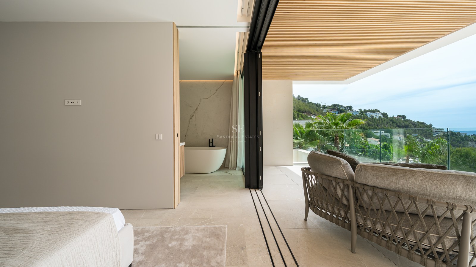 Dormitorio de lujo con bañera exenta y grandes ventanales que abren a una terraza con vistas a las colinas.