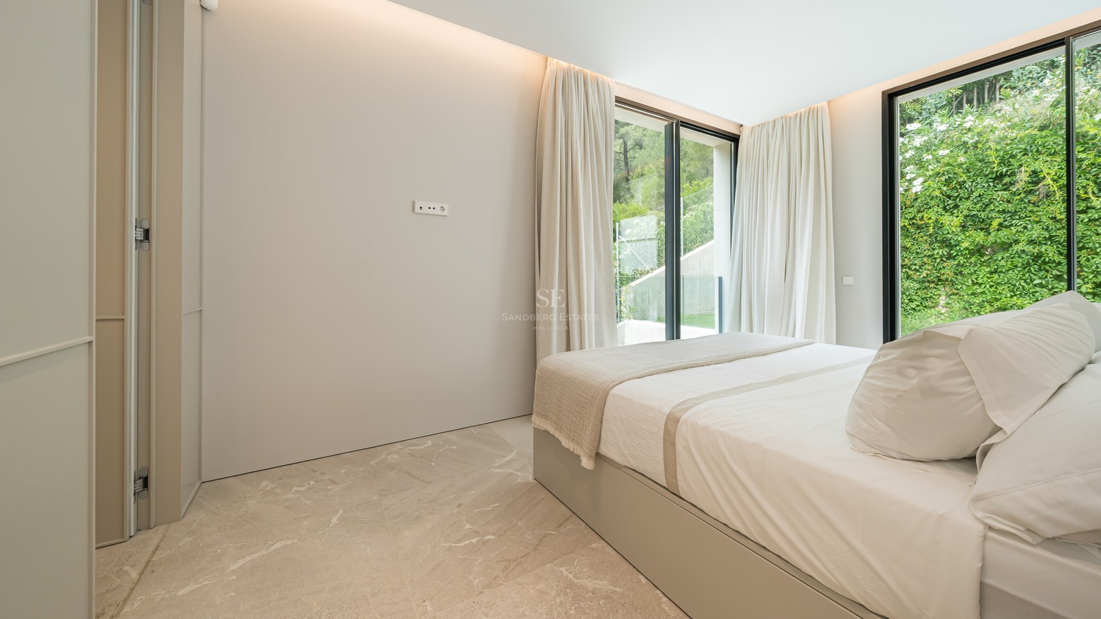 Dormitorio moderno con suelo de mármol, ventanales de suelo a techo y cama doble en tonos neutros.