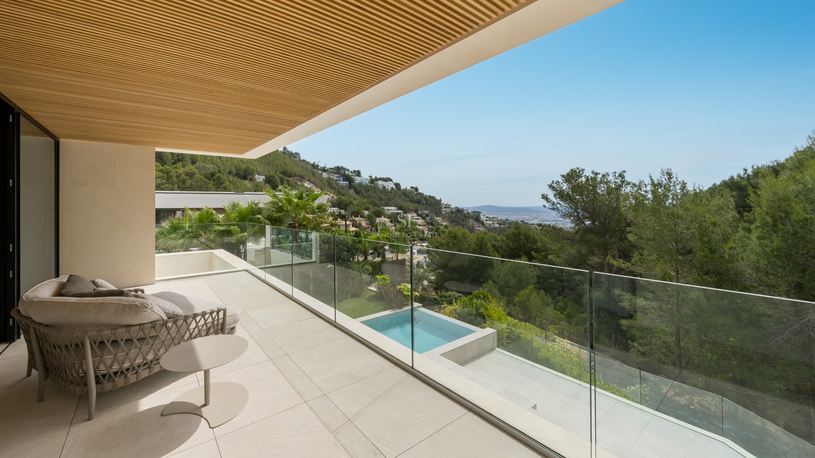 Terraza moderna con barandilla de cristal, suelo de piedra y techo de madera con vistas a la montaña y piscina.