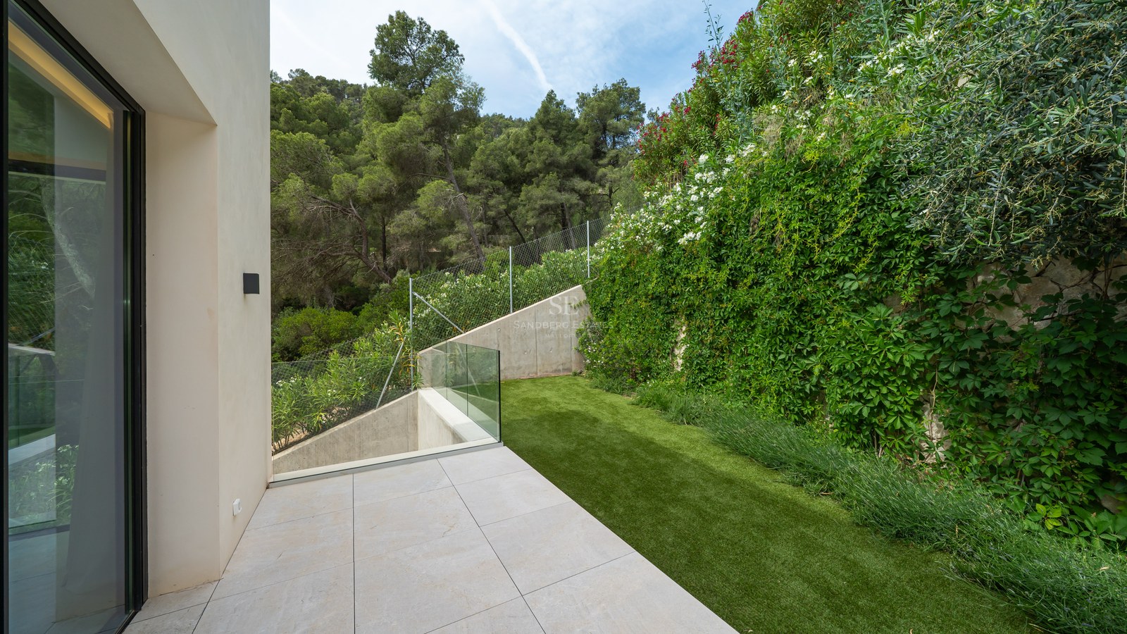 Terraza minimalista con barandilla de cristal, jardín vertical y fondo de bosque de pinos.