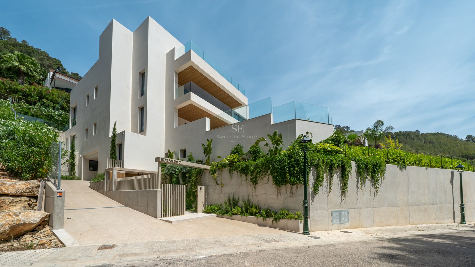 Fachada de villa moderna de varios niveles con paredes blancas, barandillas de cristal y techos de madera.