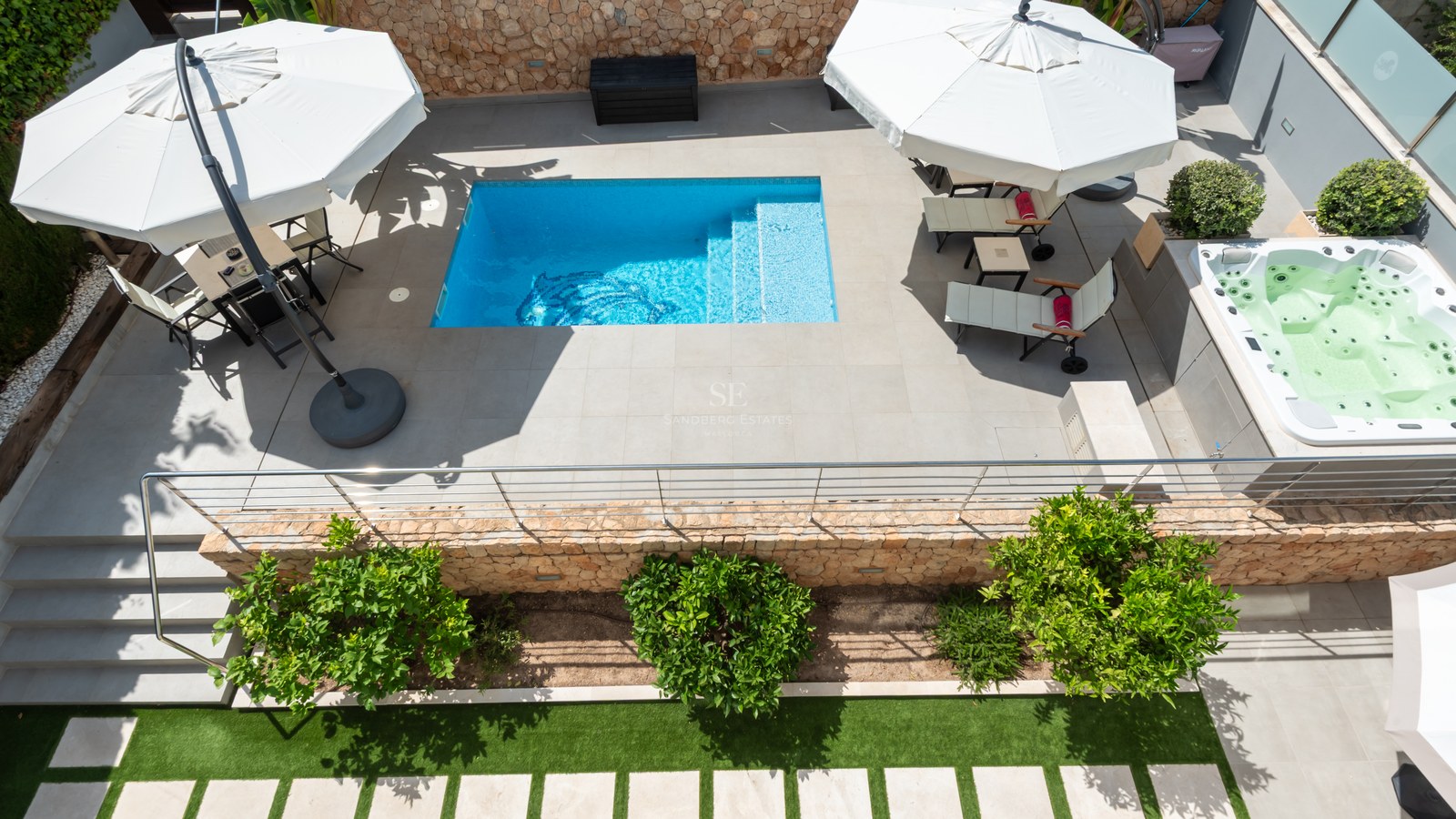 Flygvy över en turkos pool, integrerad jacuzzi och solstolar på en stenlagd terrass.