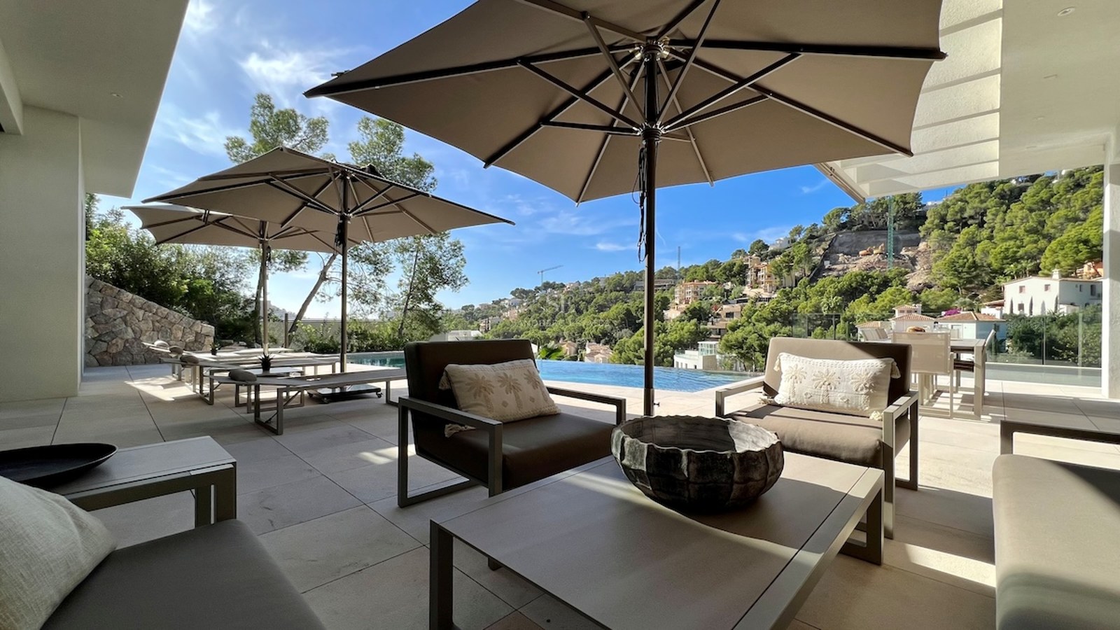 Vista del salón con piscina infinita y terraza. Arquitectura moderna, grandes ventanales, suelo de piedra y muebles de diseño.