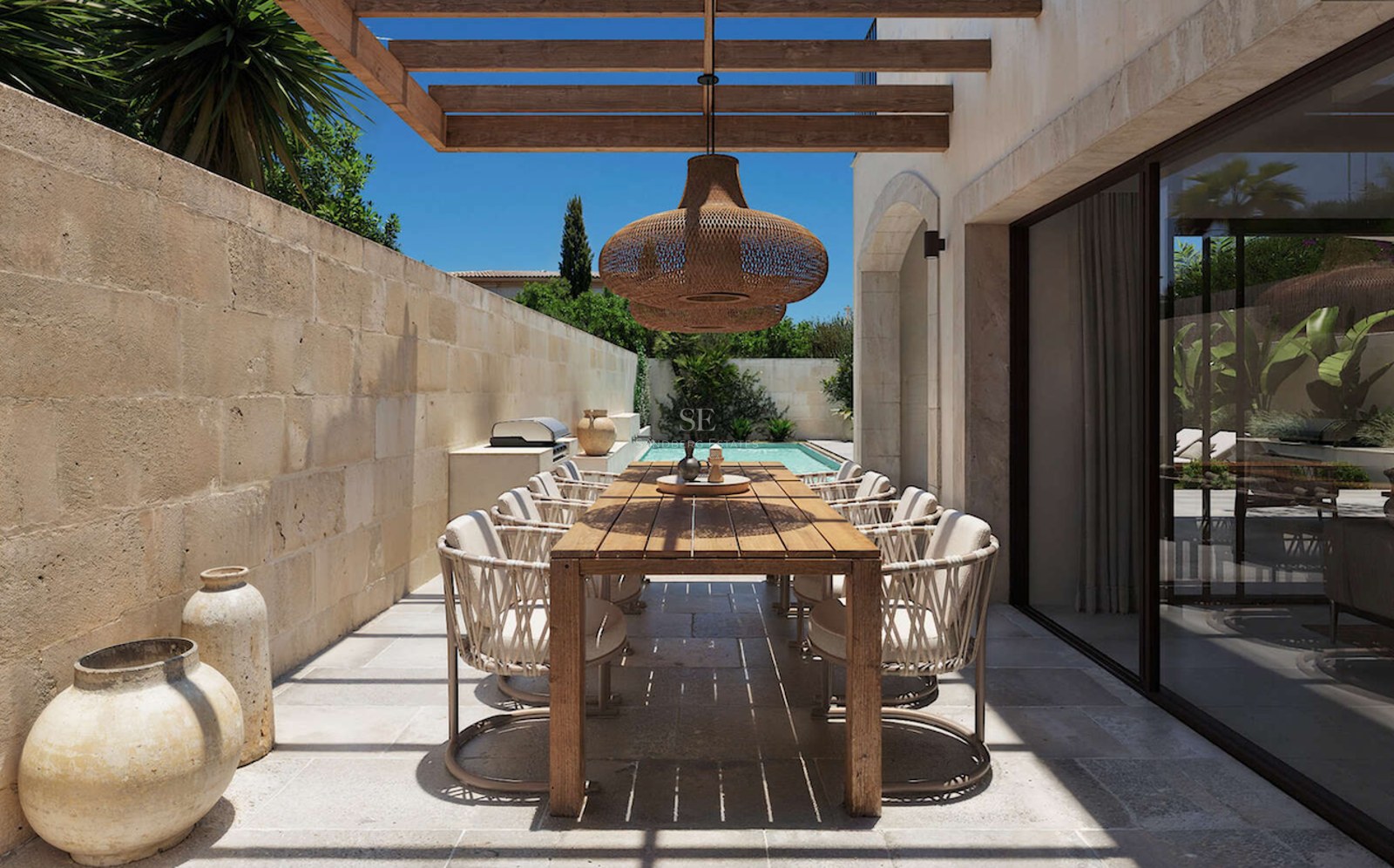 Espace repas extérieur sur une terrasse en pierre avec table en bois, pergola et petite piscine en arrière-plan.