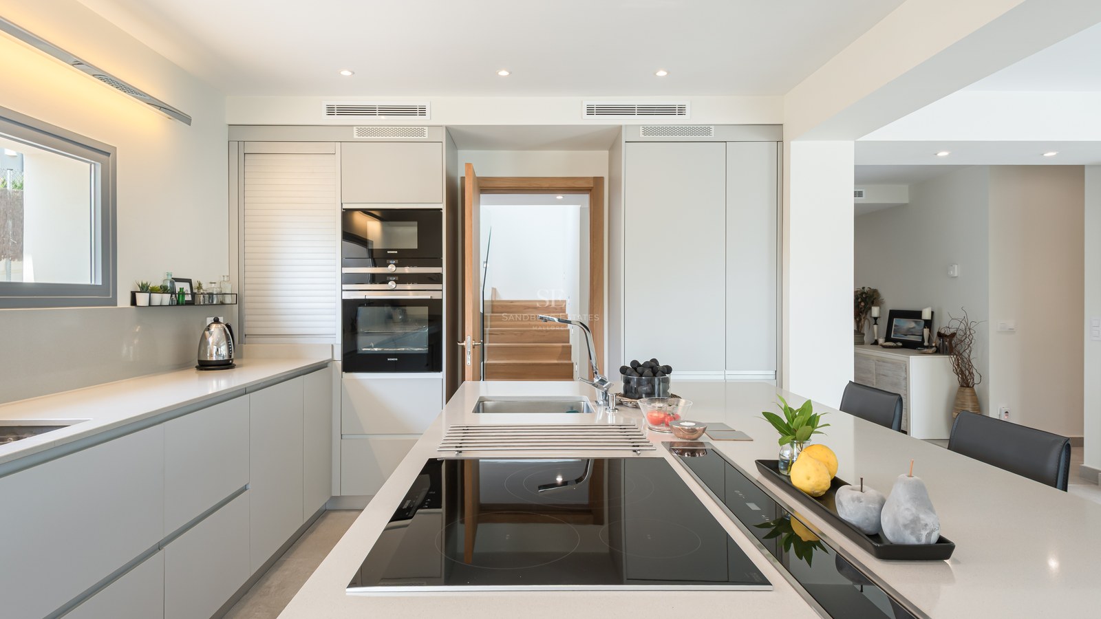 Contemporary kitchen featuring a large white island with induction hob, grey cabinetry, and built-in Siemens ovens.