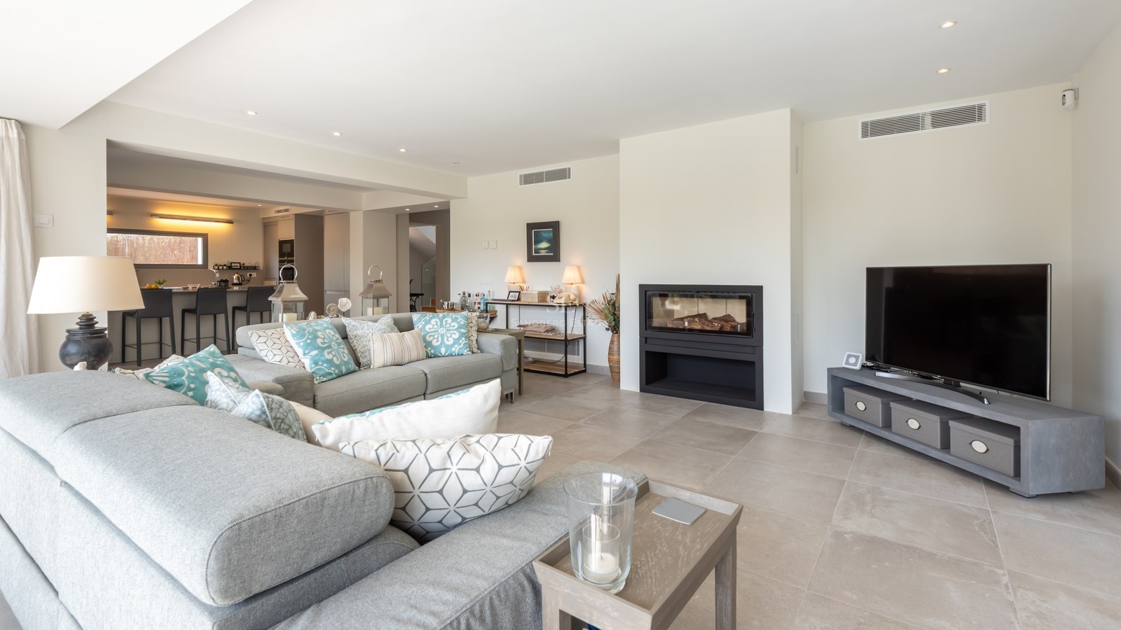 Spacious modern living room with grey sectional sofa, built-in fireplace, and views into the open kitchen.