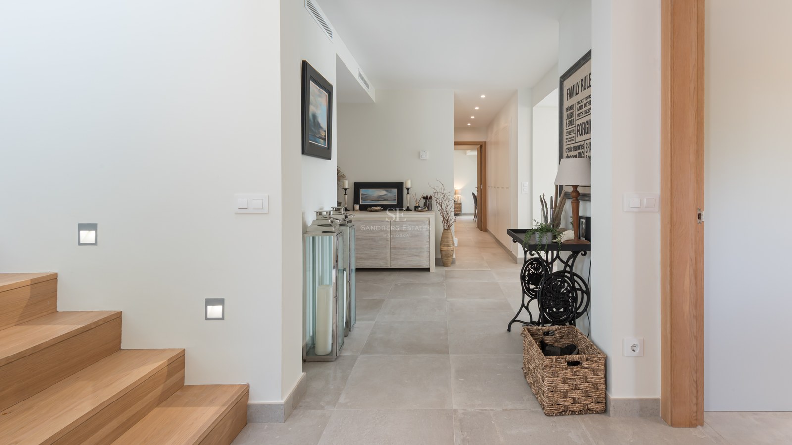 Bright entrance hallway with light wood stairs, stone tile floor, and decorative furniture in a contemporary villa.
