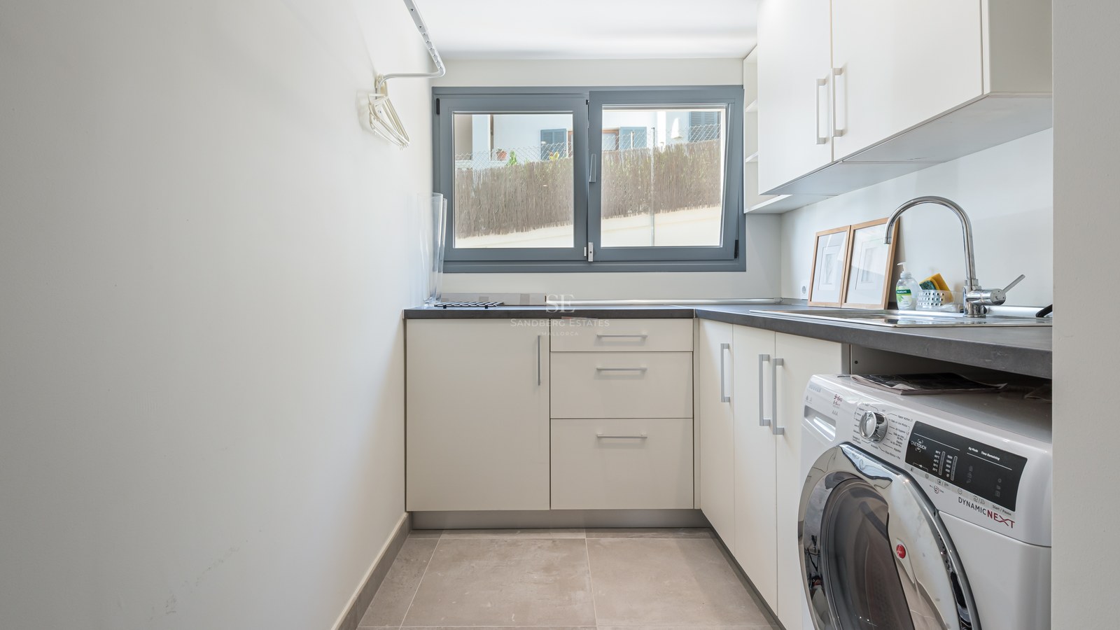 Utility room featuring white cabinetry, a grey countertop, chrome sink, and integrated washing machine under a window.