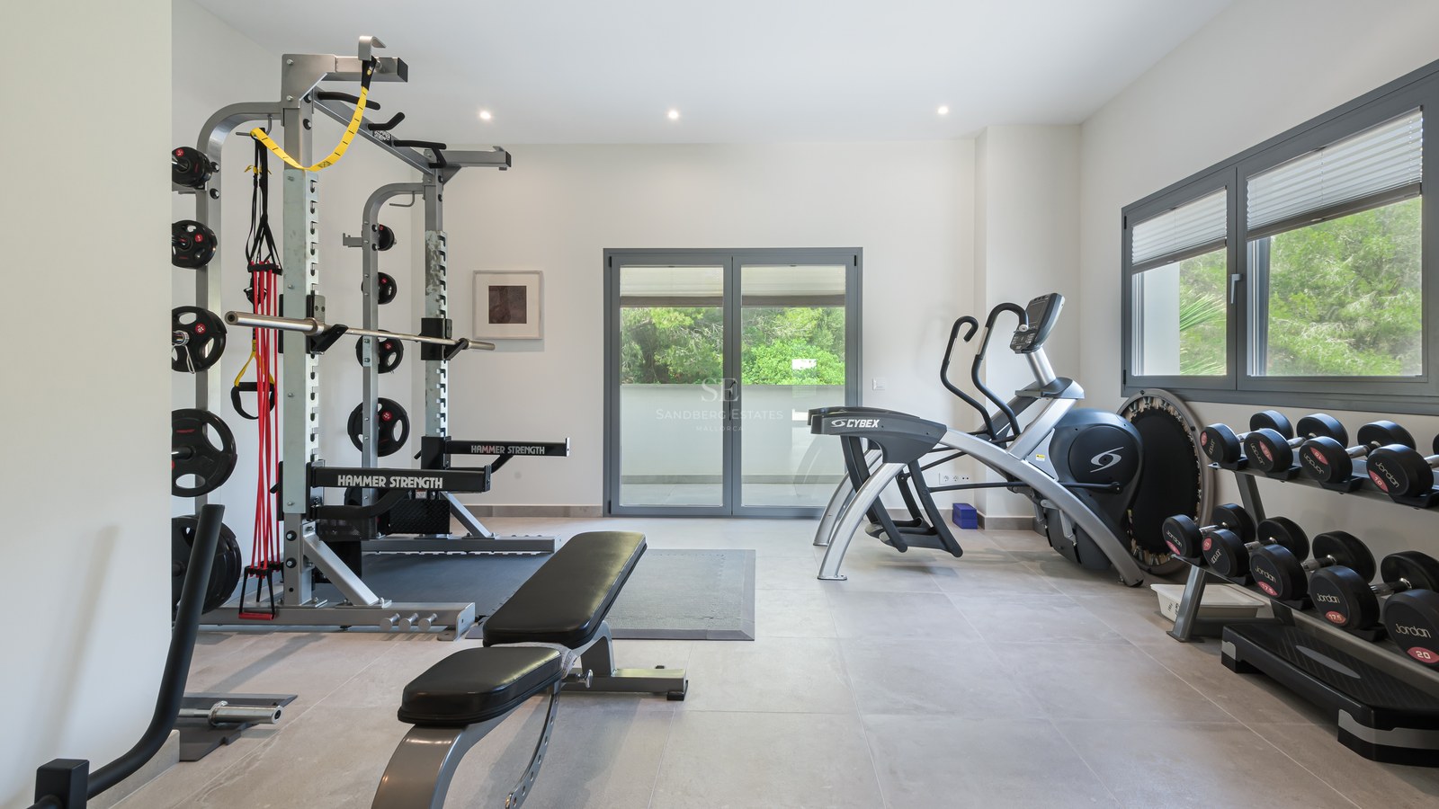Bright home gym with Hammer Strength rack, elliptical machine, and weights, featuring tiled floors and terrace access.