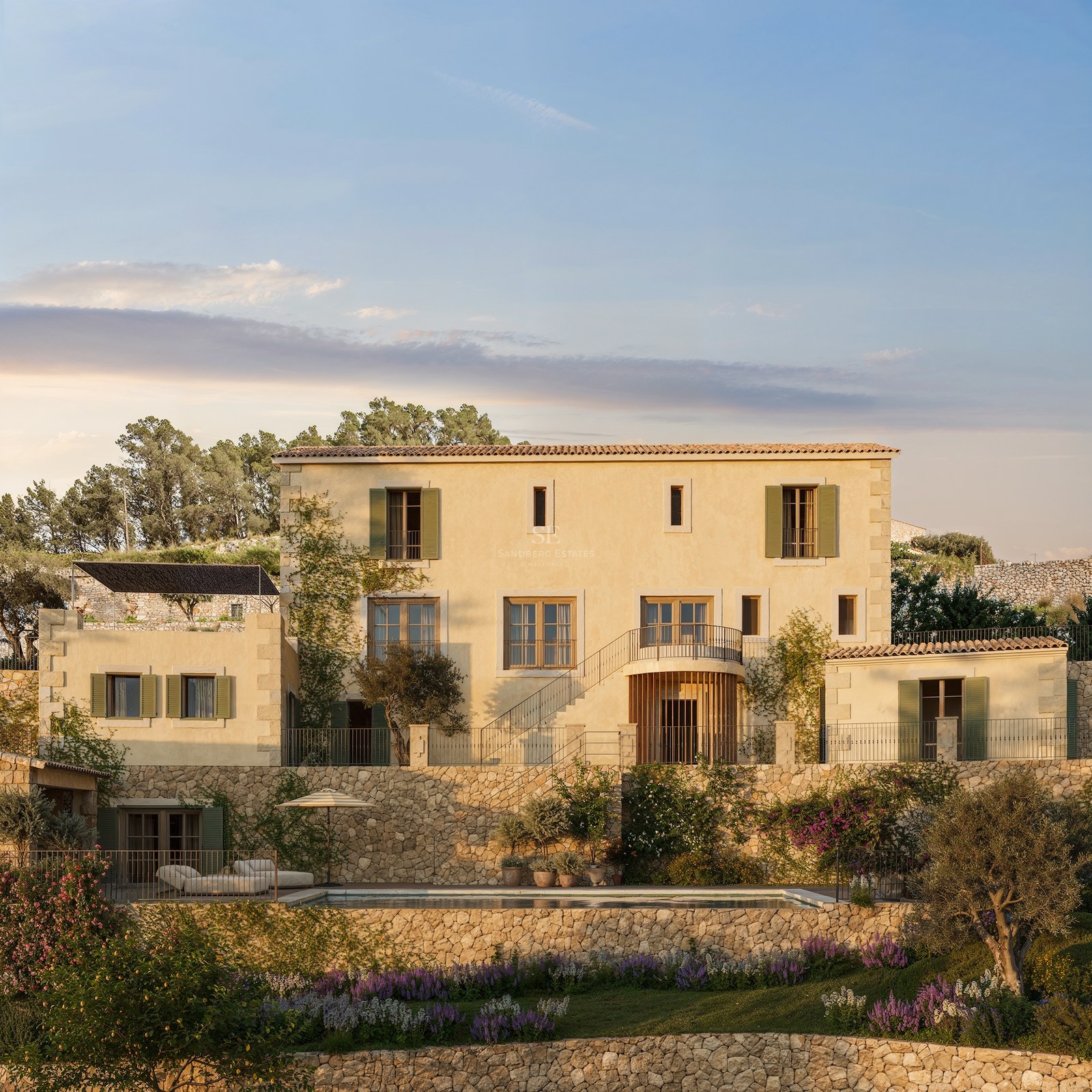 Villa méditerranéenne de trois étages avec façade ocre, murs en pierre, volets verts et piscine dans un jardin en terrasses.