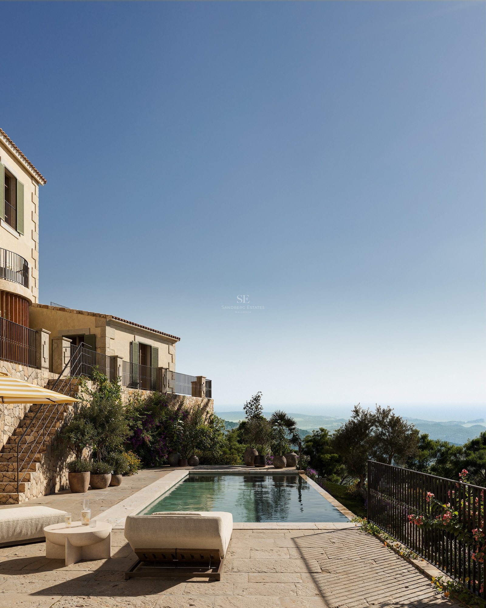 Terrasse de luxe en pierre avec piscine et chaises longues surplombant une vallée et la mer.