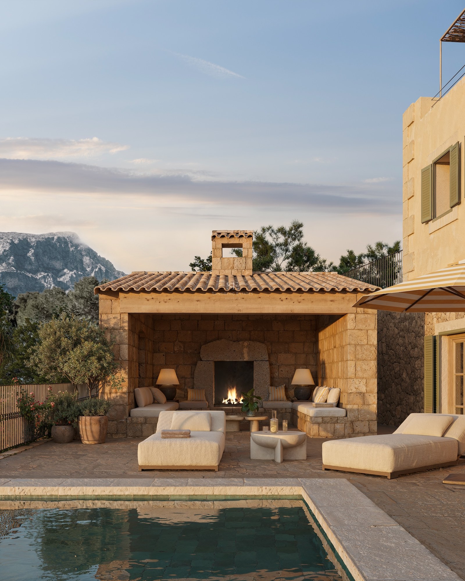 Espace piscine de luxe avec cabane en pierre, cheminée extérieure et vue sur les montagnes au crépuscule.